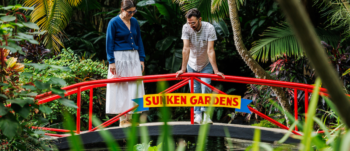 two people on bridge with sunken gardens sign