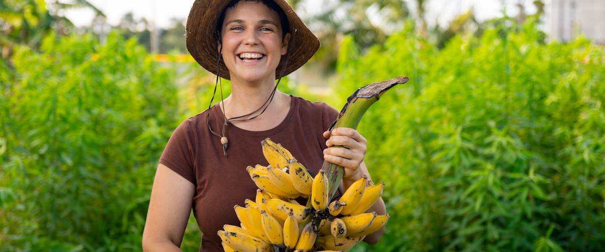 person smiling in garden holding a bundle of freshly harvested bananas
