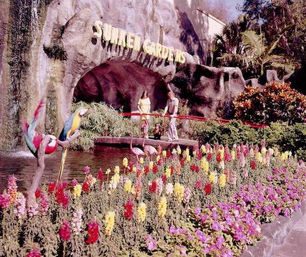 washed out photo from the 60s of two women standing in front of the Sunken Gardens cave entrance, admiring the flowers out front