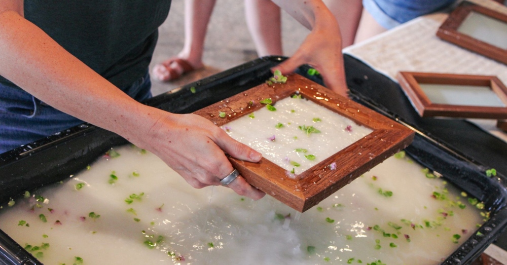 Close-up of hands sifting pulp to create homemade paper